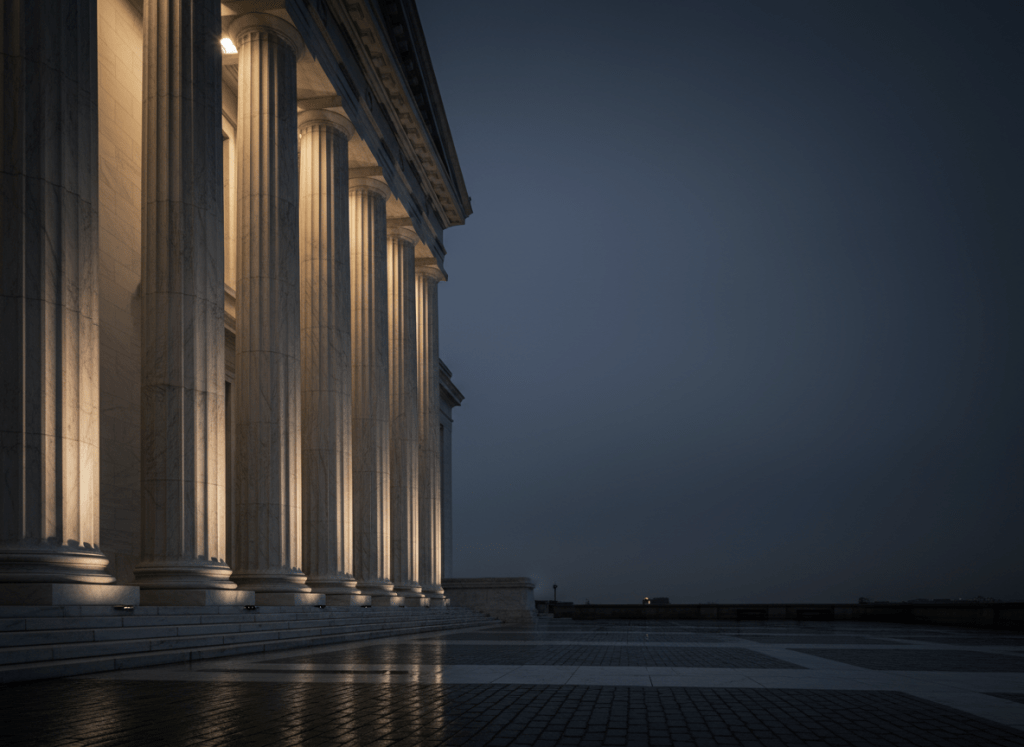 A dramatic wide-angle photograph of classic white marble courthouse columns at dusk, deep navy blue sky gradient in the background, professional legal atmosphere, cinematic lighting, dark moody tones blending to navy #0A1F3D, suitable for a law firm hero section background, ultra wide 16:9